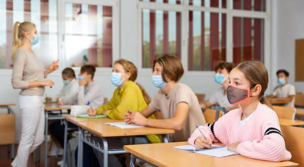 istock Schoolgirl in mask sitting in classroom 1498520438