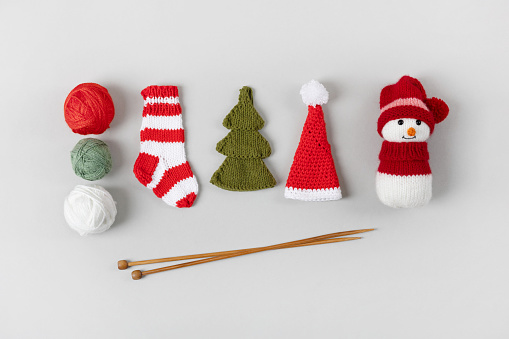 Knitting gifts for winter holidays. Knitted Christmas striped sock, snowman, Santa Claus hat and green Christmas tree with balls of thread and knitting needles. Children's toys. Top view, flat lay.