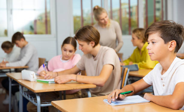istock Boy listening to lecturer and writing in notebook in classroom 1498521380