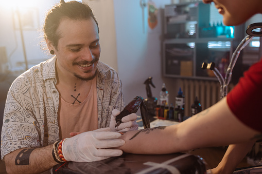 Portrait of a smiling male tattoo artist tattooing on his client's arm