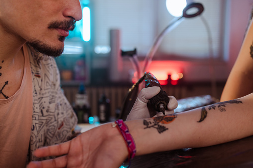 Shot of a man tattooing a flower design on his client's arm