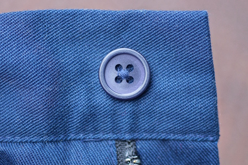 one blue plastic button on the fabric of the jacket sleeve on a brown background