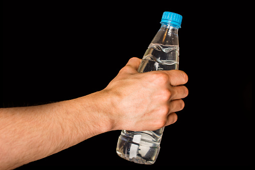 bottle with a blue lid and water in hand isolated on a black background