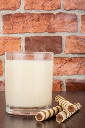 a glass of yogurt with a wafer tubule on a black background and a brick wall, free space for text, natural light