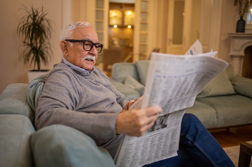 Senior man sitting and reading newspaper at home