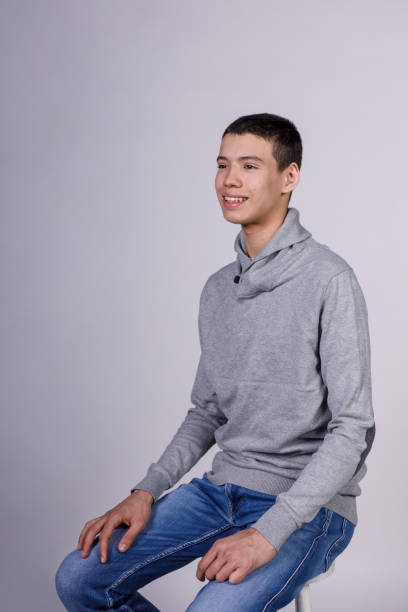 istock Charming teenage boy sitting against white background, smiling confidently 1498540052
