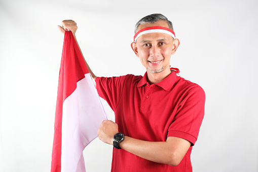 Portrait of Asian Man holding red and white Indonesia flag attribute. Independence day concept.