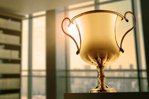 A gold trophy sits on a table in a modern office as the late afternoon sun shines through large windows.