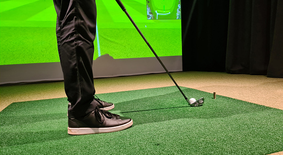 Male golfer plays golf indoors on golf simulator closeup. Driving range with screen