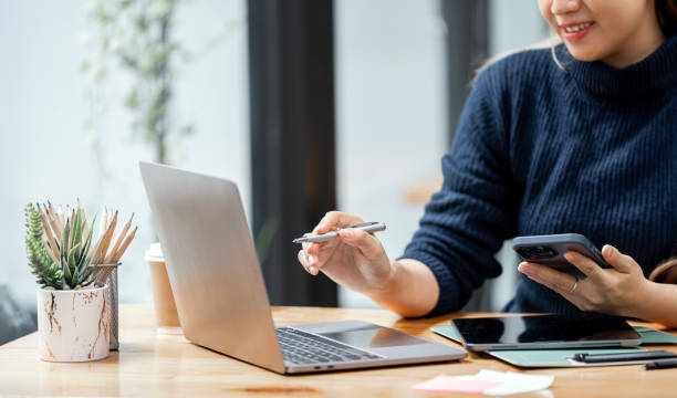istock Young woman using mobile phone and laptop computer at office. 1498577633