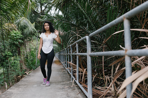 Woman waving at camera while walking down an elevated footpath in a lush tropical jungle