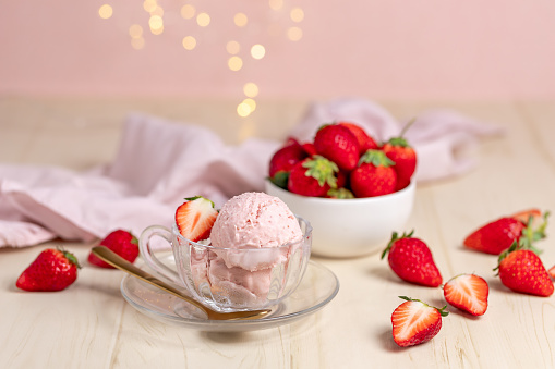 Strawberry ice cream with fairy lights on white wooden table