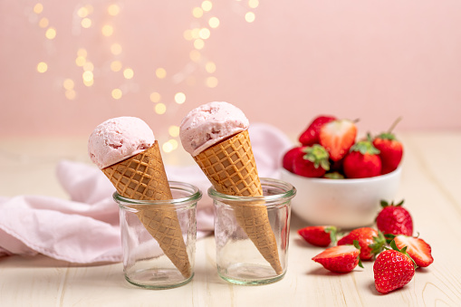 Strawberry ice cream cones with fairy lights on white wooden table