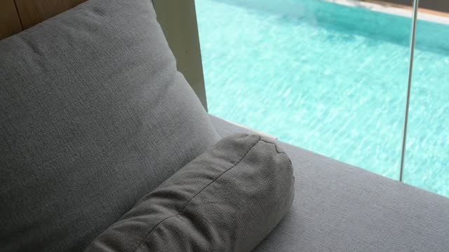 gray pillow put on bed, swimming pool view and slow motion water wave