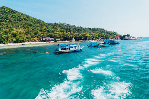 In Koh Tao, Thailand a wooden boat equipped with scuba diving tanks drives in the water surrounding the island. The Padi logo is painted on the side.