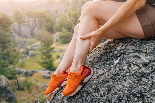 A girl massages the calf of her leg after an injury or stretching of a muscle during a hike