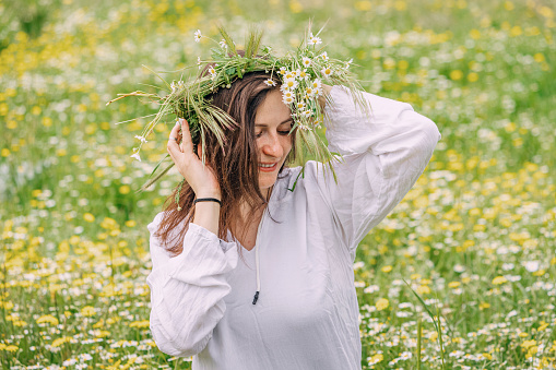 Happy girl in chamomile flower wreath at natural meadow outdoors