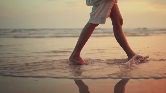 B roll - Woman feet walking along sea water waves on sandy beach in sunset, Female tourist on summer travel vacation, Slow motion