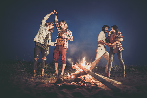 Young happy couples having fun while dancing on a beach party by the campfire.