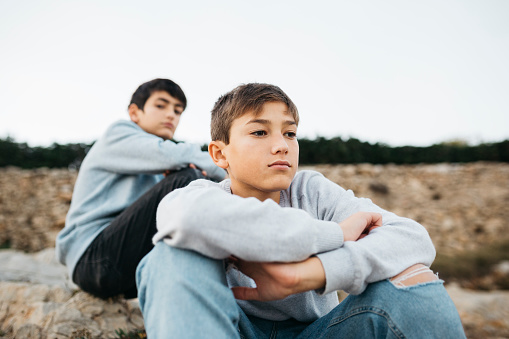 Two male brothers hanging out on a rock breakwater, next to the sea