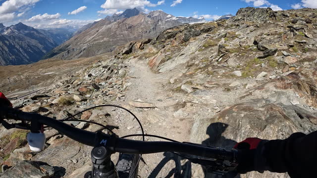 POV of a mountain biker riding along a trail in the mountains on a sunny day