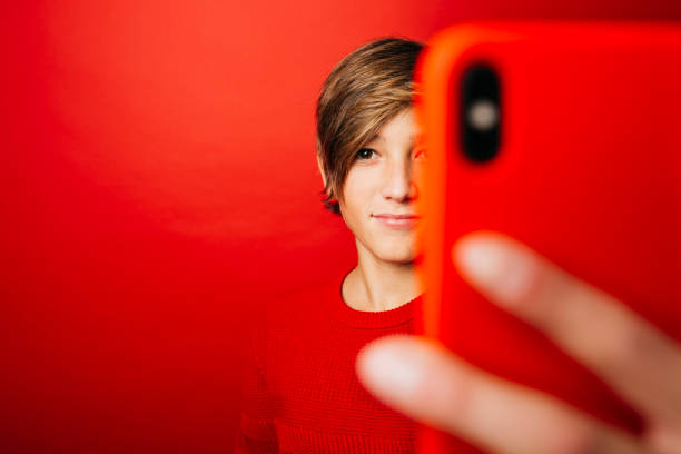 Pre-adolescent boy taking a selfie over a red background