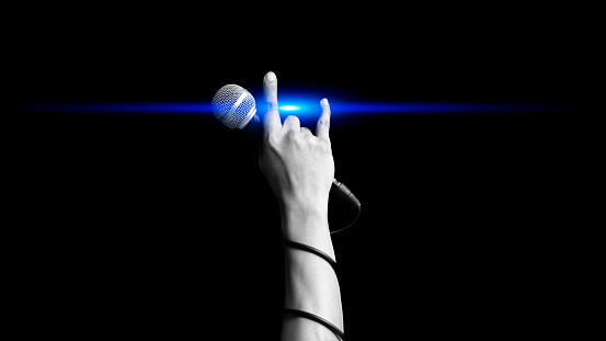 close up microphone in hand sign of singer raised his hand all the way up with blue light showing power, hope and love in live concert