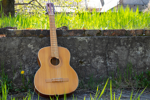 wooden brown guitar lies on a stone road in the street in the spring grass