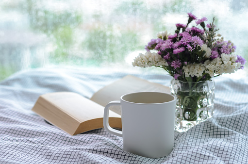 A cup of coffee with book on bed in morning with rain drop on window. Stay home and relaxing concept