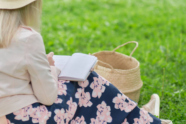 istock woman with pen writing on notebook on grass outside. 1498618608