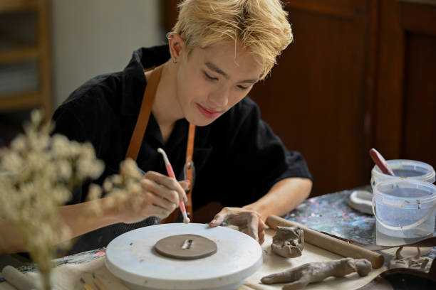 istock A creative Asian gay man pottery artist holding a sculpting tool, making patterns on raw clay 1498618682