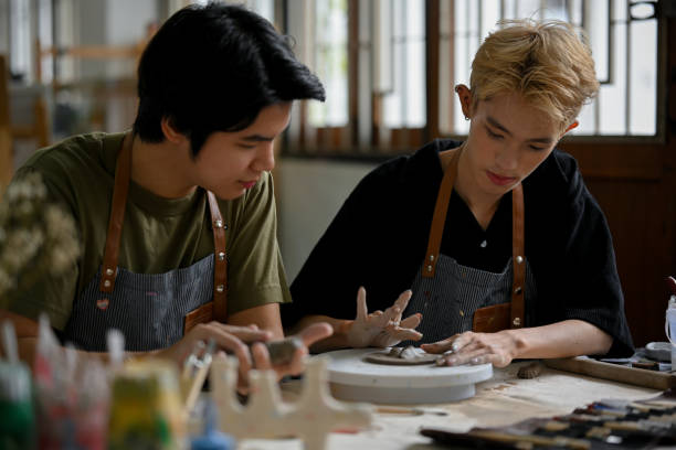 A man molding clay, making a handmade clay ornament in a workshop with his friend.