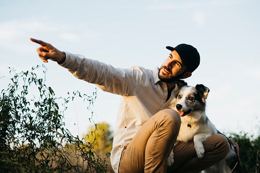 Portrait of a young bearded man wearing a black cap, with his dog, at countryside