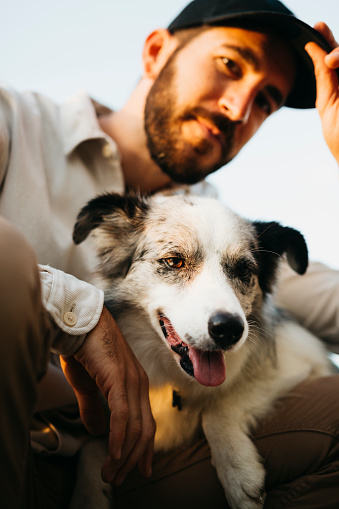 Portrait of a young bearded man wearing a black cap, with his dog, at countryside