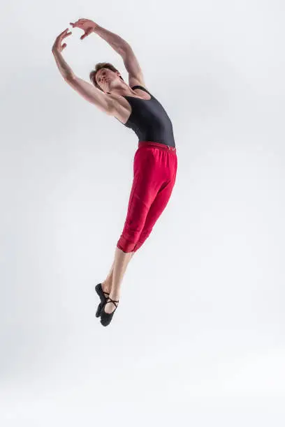 Young Flexible Athletic Man Posing in Red Tights in Flying Dance Pose With Hands Connected in Studio on White.Vertical Composition