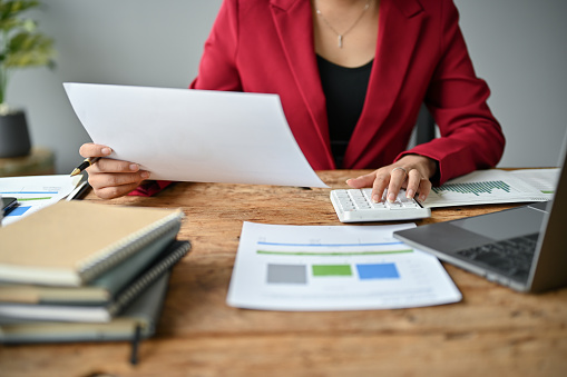 Close-up image of a professional Asian businesswoman using a calculator to plan budgets and working on financial reports at her desk.