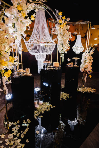 Delicious luxury wedding reception. Birthday Cake on party. Celebration concept. Candy bar. Table with sweets, candies, dessert. Arch with large chandelier, flowers, candles, rose petals on floor hall