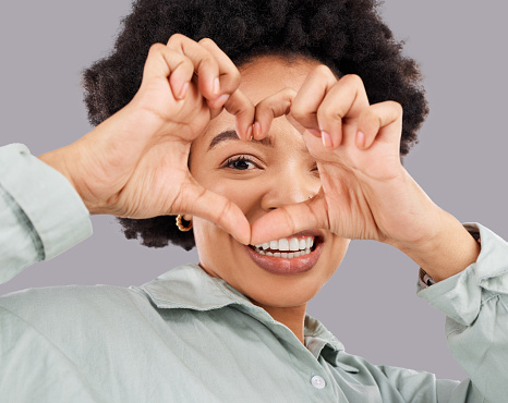 Heart, eye and hands with portrait of black woman in studio for happiness, support and emoji. Peace, focus and shape with female holding symbol on gray background for hope, kindness and trust
