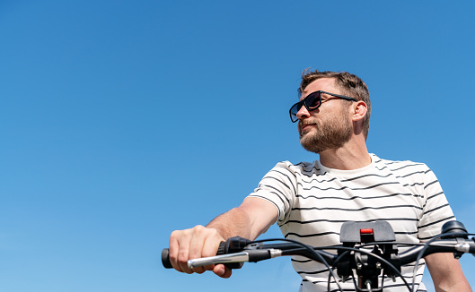Man wearing sunglasses sits on the bicycle on background of blue sky.