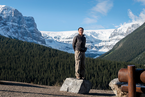 Tourist standing on a rock with snow-capped mountains in the background. Jasper National Park, Alberta, Canada.