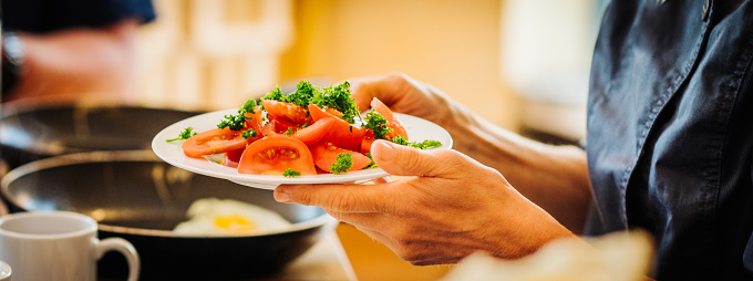 Hands holding a plate of healthy tomatoes, tomato salad with parsley. Panoramic, selective focus on individual tomatoes