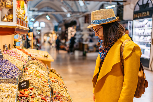 Beautiful young woman looking at dried tea mixtures and leaves at the Grand Bazaar In Kapali Carsi in Istanbul, Turkey.