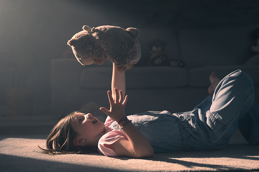 Child playing and talking to plush toy. Little girl holding teddy bear with sunset light at home.