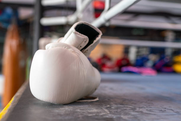 Photo of a pair of white boxing gloves on the floor of a boxing ring in a gym