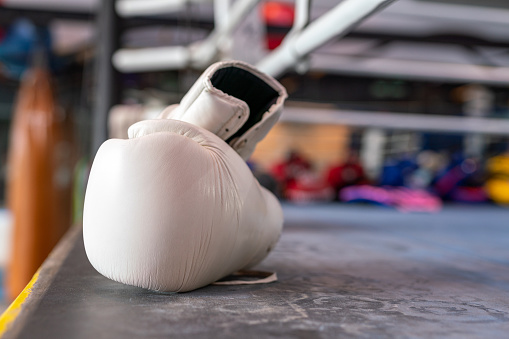 Photo of a pair of white boxing gloves on the floor of a boxing ring in a gym