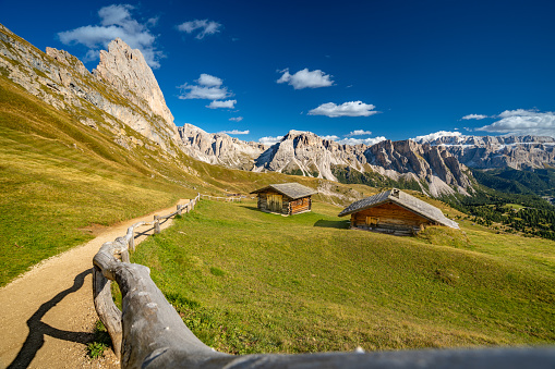 wooden fence along mountain pasture with two old huts in beautiful alpine landscape high up in the seceda mountains in then dolomites on sunny day