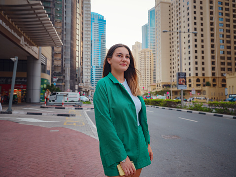 young woman in green suit walks streets of Dubai, Dubai Marina district. United Arab Emirates trip concept. the idea of successful expat, moving to another country, work visa