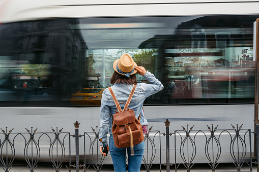 Rear-view of a young woman waiting for a tram in Istanbul, Turkey. A tram passing in front of her, blurred motion.