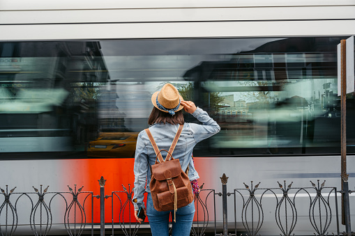 Rear-view of a young woman waiting for a tram in Istanbul, Turkey. A tram passing in front of her, blurred motion.