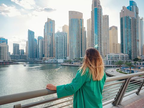 young woman in green suit walks streets of Dubai, Dubai Marina district. United Arab Emirates trip concept. the idea of successful expat, moving to another country, work visa